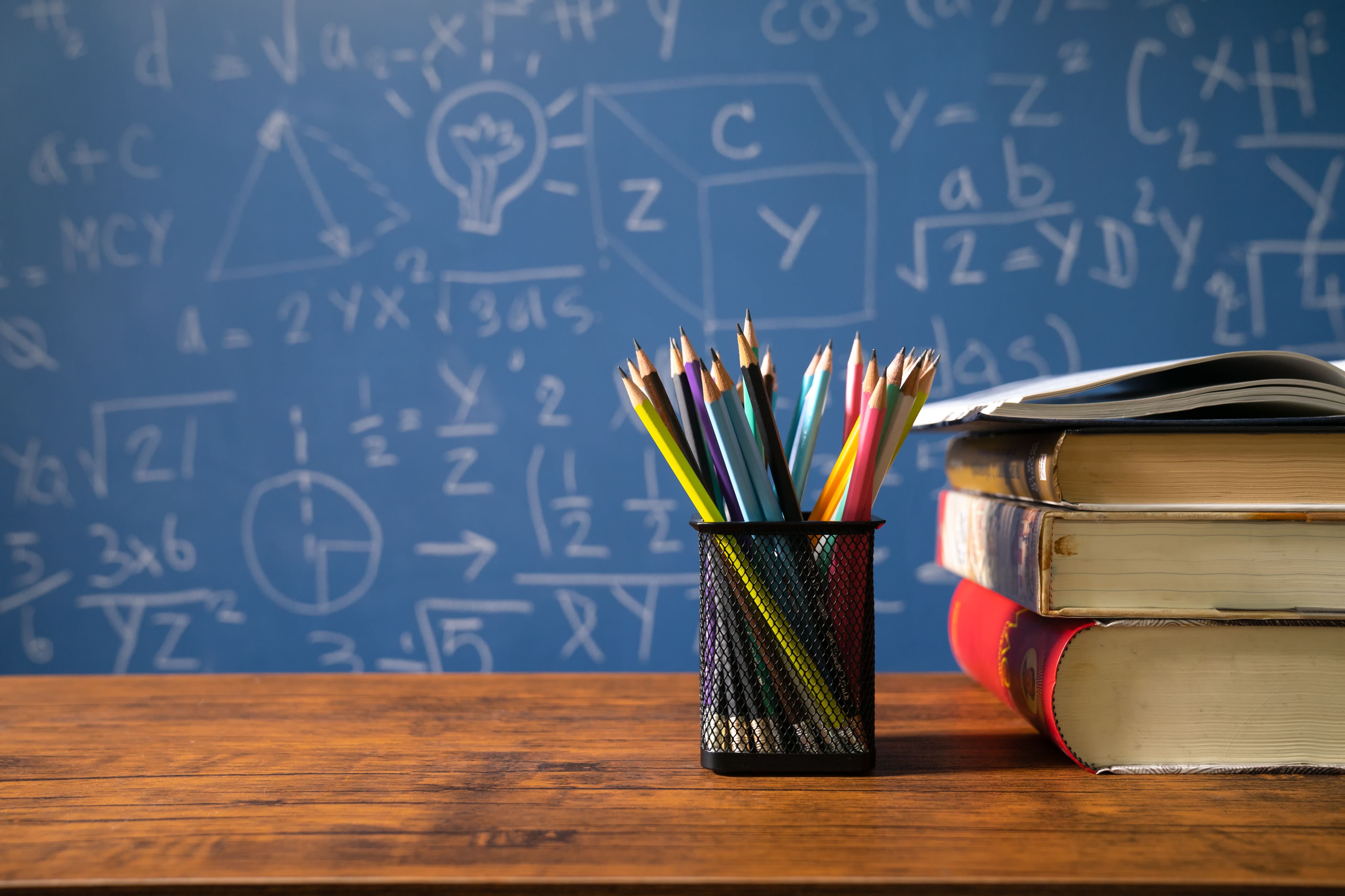 Teacher's desk with school supplies on top and blackboard in background.